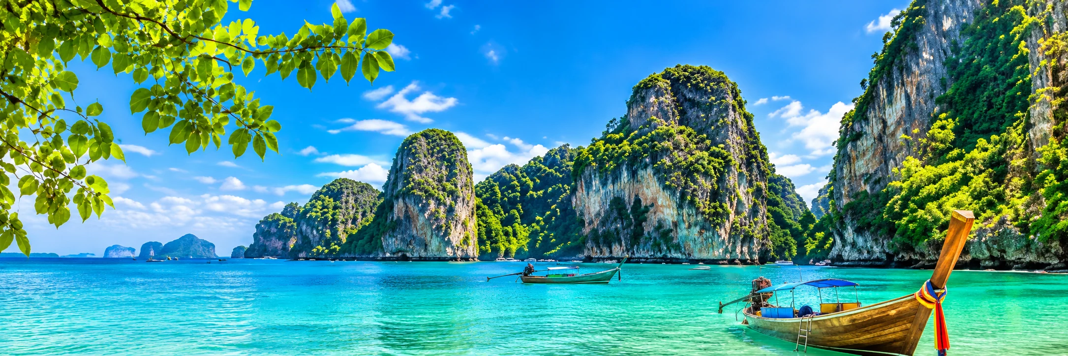 Türkisfarbenes Meer, grüne Kalksteinfelsen und ein traditionelles Longtailboot in Thailand
